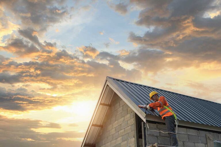 A person inspects shingles on a residential roof with visible patches and repair materials nearby.