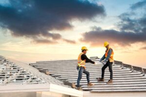 Worker applies a white protective coating across a low-slope roof beside repair tools and drainage vents.