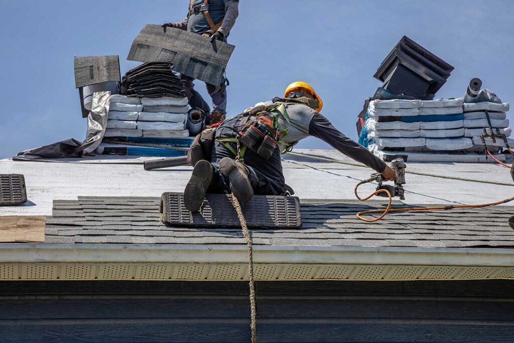 A person in safety gear using a ladder to carefully access a shingle roof on a house.
