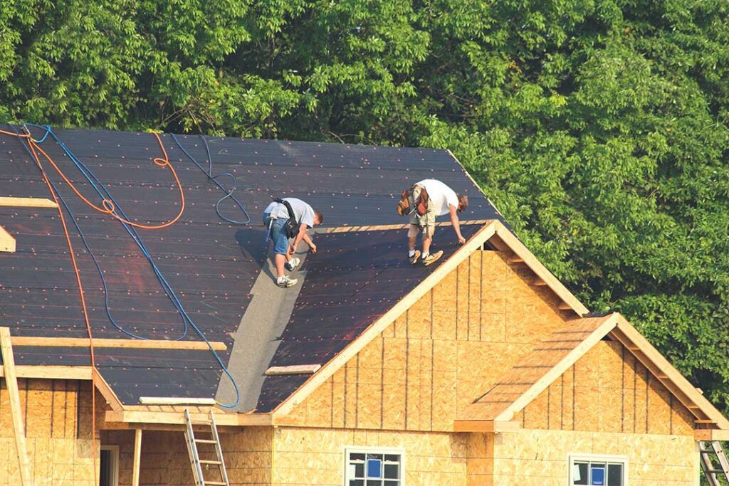 A light-colored residential roof reflects bright summer sunlight above an insulated attic.