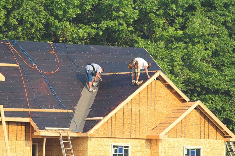 A light-colored residential roof reflects bright summer sunlight above an insulated attic.